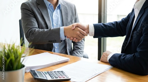 Two businessmen shaking hands, sealing a deal after a successful negotiation in an office.