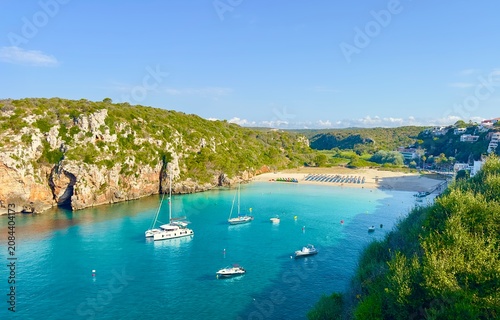 A beautiful view of the beach and turquoise waters in the bay on a summer's morning at Cala en Porter on the Balearic Island of Minorca, Spain. 