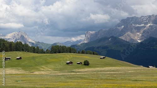 Fotografie Scenic alpine meadows and traditional wooden cabins beneath dramatic Dolomite peaks at Alpe di Siusi, Italy