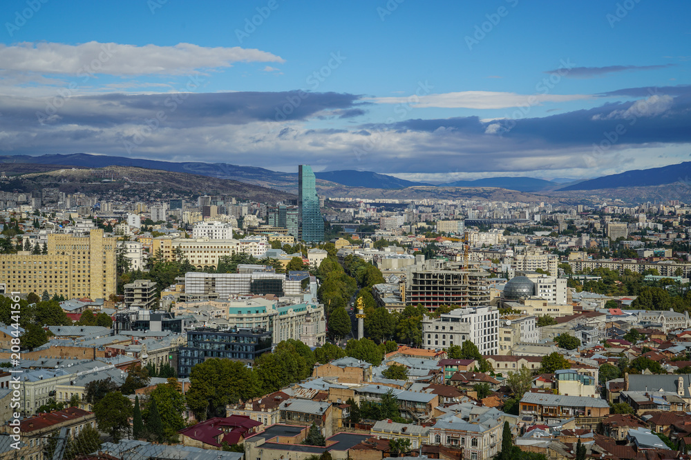 Fototapeta premium Expansive panoramic view of Tbilisi cityscape in Georgia with Biltmore Hotel skyscraper under a partly cloudy sky