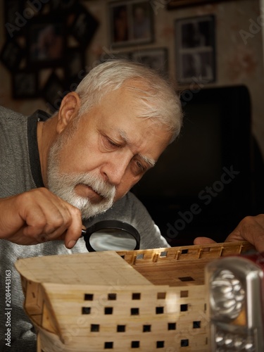 Foto Elder man examines a basket with a magnifying glass in his home during the after