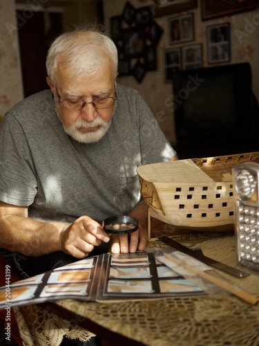 Elderly man looks at old photos with a magnifying glass in a cozy room surrounded by memories
