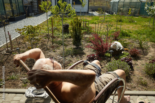 Man sits in wheelchair in garden while cat relaxes nearby under sunlight in spring