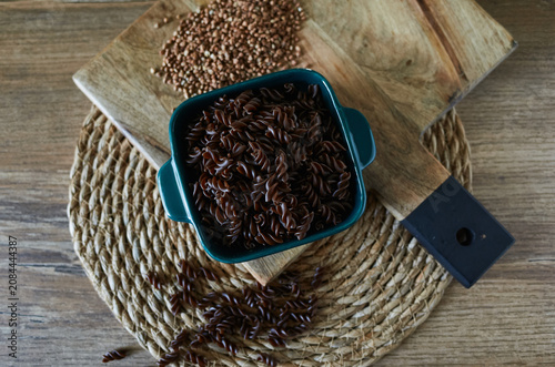 Bowl of dark pasta on a wooden cutting board with seeds in the background on a kitchen table