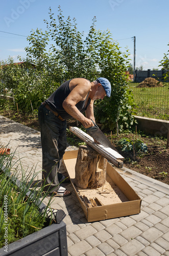 Man cuts wood for a project outside in sunny weather with trees and grass in the background