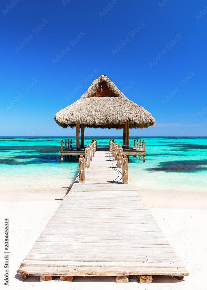 Fototapeta premium Luxury tropical beach scene at Cap Cana in the Dominican Republic featuring a wooden pier, turquoise Caribbean Sea and traditional gazebo.