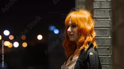 Portrait of a beautiful fiery red-haired woman on a city street at night.