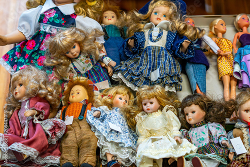 Quadro su tela Close-up of a collection of antique porcelain dolls dressed in ornate vintage clothing, sitting in a wooden crate, detailed faces and hair, arranged in a group on display, visible price tags
