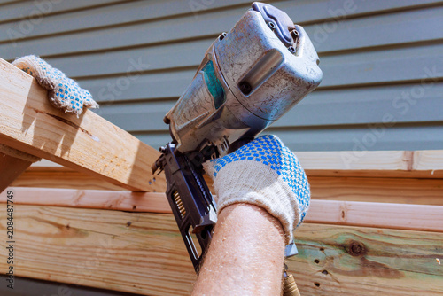 Hand is holding air nail gun while working on wooden structure