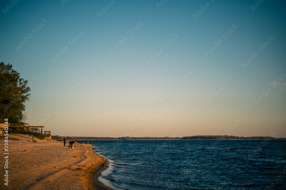 Obraz premium Golden hour on a sandy beach with calm blue water and distant treeline