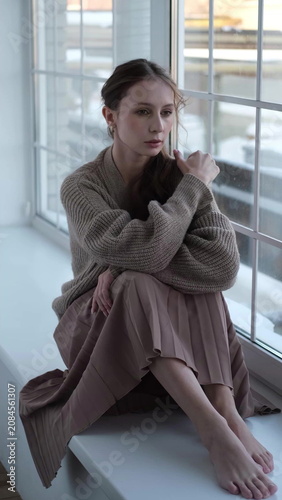 Beautiful young girl posing for the camera while sitting near a large window