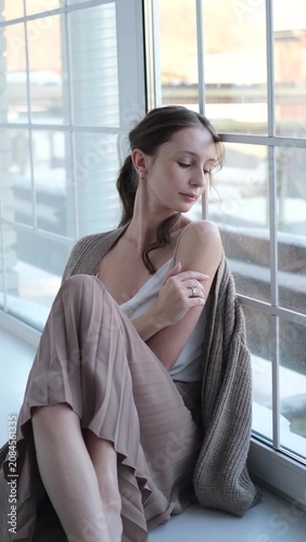 Beautiful young girl posing for the camera while sitting near a large window