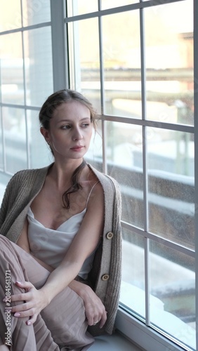 Beautiful young girl posing for the camera while sitting near a large window