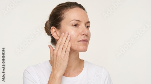 Woman applying facial cream for skincare routine on a white background