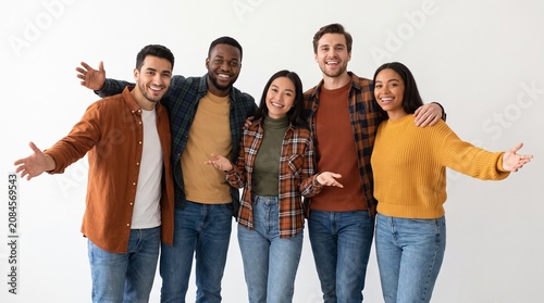 Diverse group of five young friends smiling and gesturing welcomingly