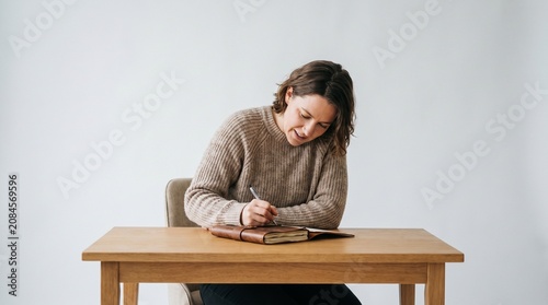 Woman writing in a leather bound journal at a wooden desk