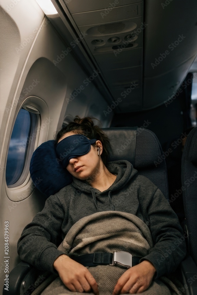 Fototapeta premium Young traveler sleeping on airplane with eye mask and blanket