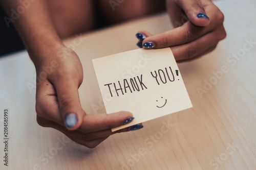 Heartfelt gesture captured in a close up of hands presenting a thank you note adorned with a smiley face