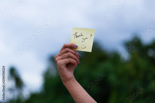 A hand presenting a sticky note featuring a thank you message set against a serene nature backdrop