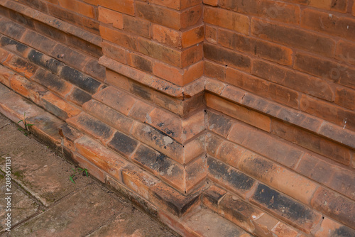 Ancient Red Brick Corner Detail of Temple Wall. A weathered red brick wall, featuring tiered molding and rustic clay textures