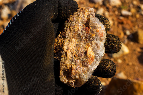 фотографія Gloved hand holding a raw granite pegmatite specimen, detailed texture of quartz