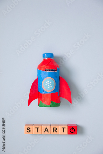 Creative startup concept with handmade rocket, wooden START blocks on blue background, symbolizing business growth, innovation, entrepreneurship, motivation, success.