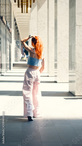 A portrait of a teenage girl with red hair posing for a photo near columns at the entrance to a business center