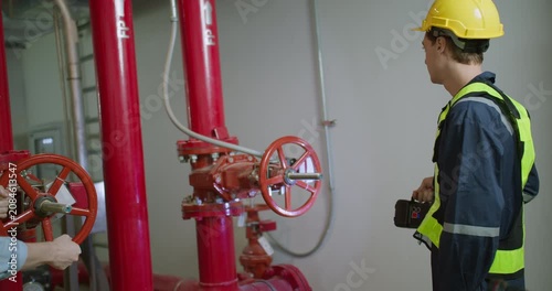 An industrial engineer performs a safety inspection, turning a valve on a fire suppression system to ensure operational compliance within a factory plant room.