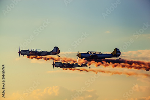 Propeller planes flying in formation leaving smoke trails at sunset