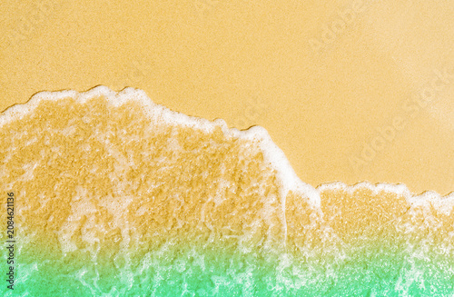 Obraz na płótnie Top view of gentle ocean waves washing onto golden sandy beach with turquoise tropical water, creating a clean natural background for summer travel, coastal tourism, relaxation, and vacation concepts