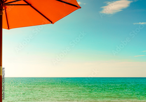 Tableau sur toile Orange beach umbrella overlooking the turquoise tropical ocean beneath blue sky