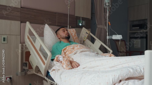 Male patient resting and recovering in a modern hospital room with IV drip, medical bed, and healthcare equipment, representing treatment, recovery, and medical care.