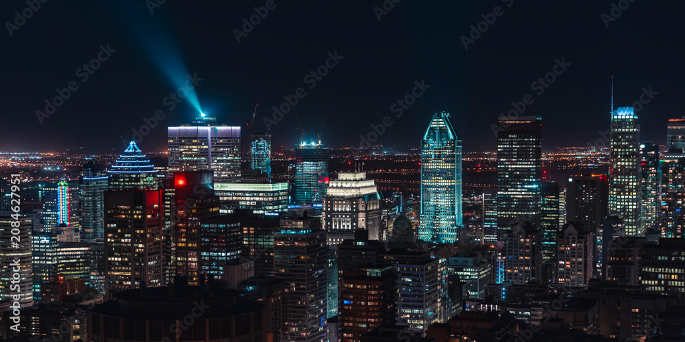 Fototapeta premium Montreal downtown skyline illuminated at night with glowing skyscrapers and a bright light beam over the financial district, Quebec, Canada