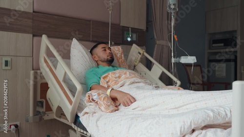 Male patient resting and recovering in a modern hospital room with IV drip, medical bed, and healthcare equipment, representing treatment, recovery, and medical care.