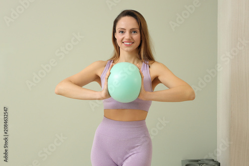 Young woman holding green fitness ball in purple sportswear