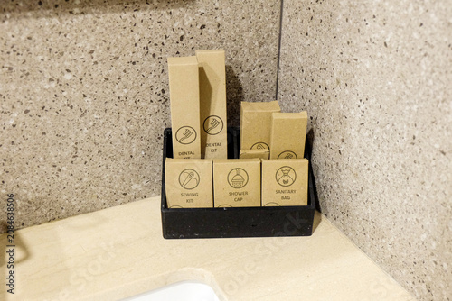 ollection of hotel amenities, including a dental kit, shower cap, sewing kit, and sanitary bag, neatly packaged in brown kraft paper boxes inside a black holder.