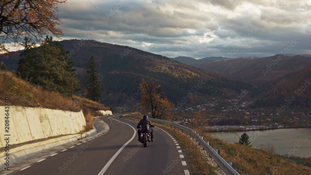 Fototapeta premium Motorcyclist riding winding mountain road enjoying scenic autumn landscape
