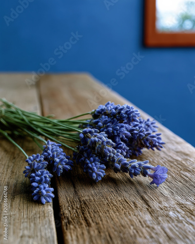 Fresh lavender flower bouquet on rustic wooden table, blue wall background, natural light, calming mood, aromatic herb, countryside style