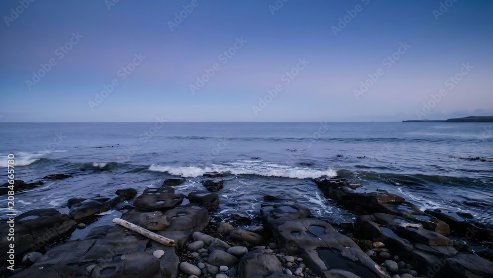 Fototapeta premium Calm ocean waves gently lapping against a rocky shoreline under a dusky sky