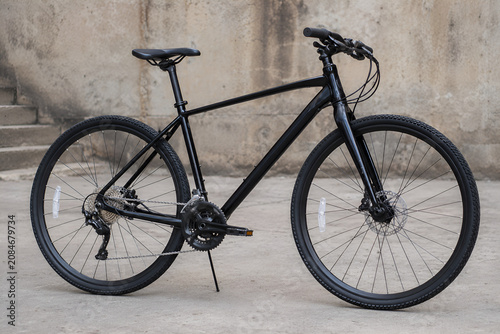 Minimalist Matte Black Hybrid Bicycle with Disc Brakes Parked Against an Urban Concrete Wall in Modern Lifestyle Style