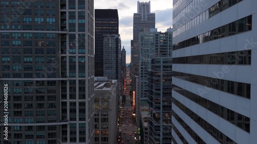 Urban canyon street in Chicago leading to historic Chicago Theatre marquee, downtown neighborhood architecture and cityscape with traffic below at twilight