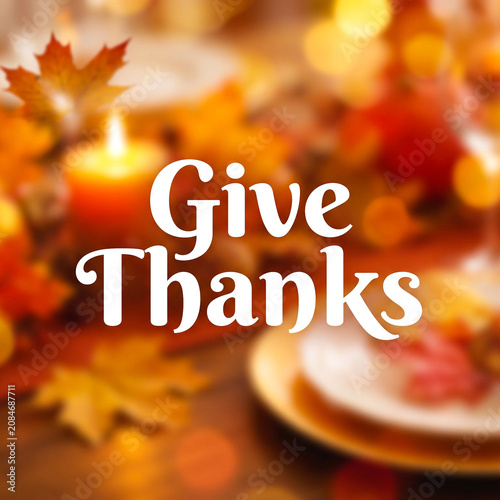 Give thanks text over a blurred thanksgiving table setting with a candle and autumn leaves