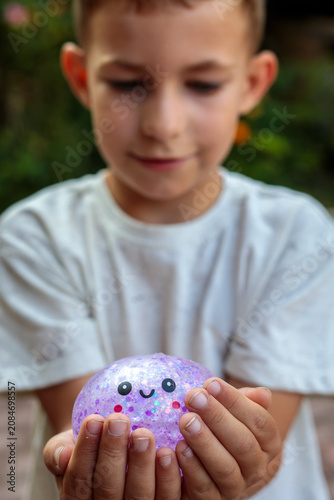 фотографія Smiling little boy playing with a glittery dumpling shaped squishy toy outdoors,