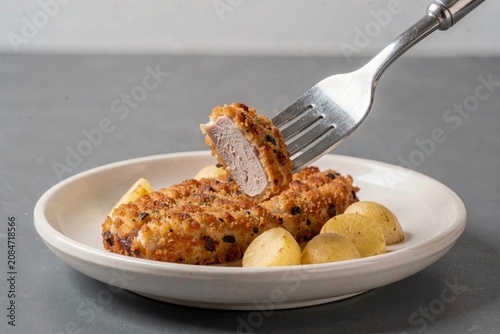 Kotlet Schabowy, breaded pork cutlet served with neat round roasted potatoes in white bowl. Concept of savory breaded pork cutlet with potatoes salad on grey surface.