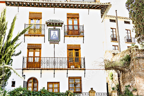 White Andalusian-style facade with wrought-iron balconies decorated with flowerpots, Granada, Andalusia, Spain