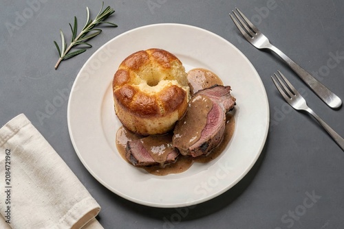 Yorkshire Pudding topped with pork tenderloin, fluffy and golden brown, garnished with rosemary. Concept of batter pudding served with roast beef, perfect for dining.