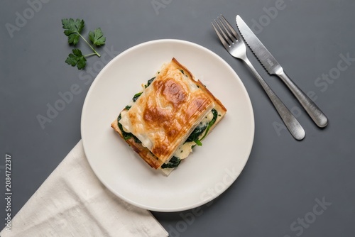 Zeljanica on white plate, slice of phyllo pastry with spinach cheese filling, garnished with fresh parsley. Concept of savory baked pastry dish, perfect for meals or snacks.
