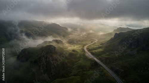 Winding road through a misty mountain valley under dramatic cloudy skies