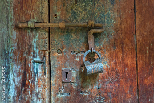 Old sliding bolt lock with padlock on antique wooden door
