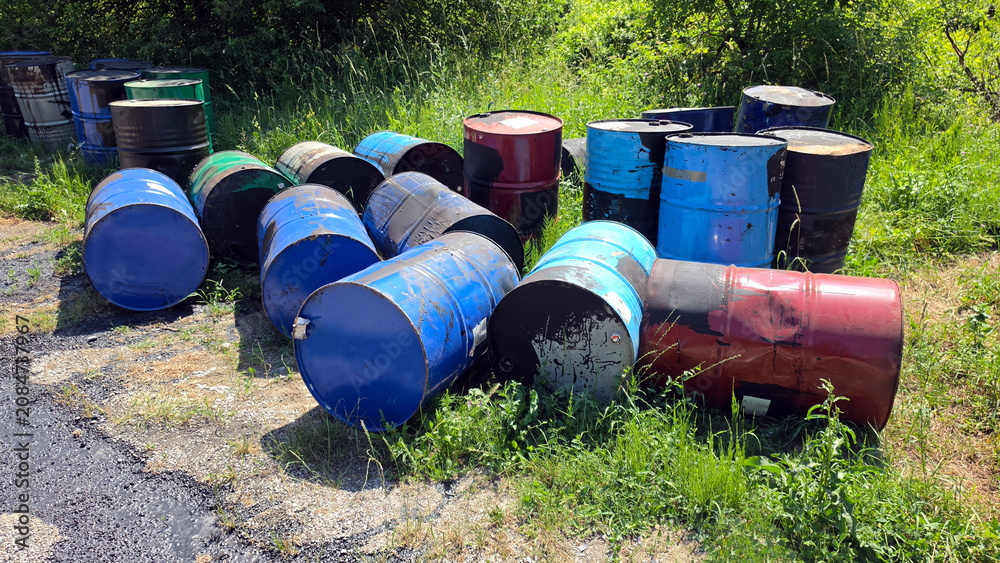 Fototapeta premium Ecological hazard of discarded industrial oil drums polluting a green roadside field